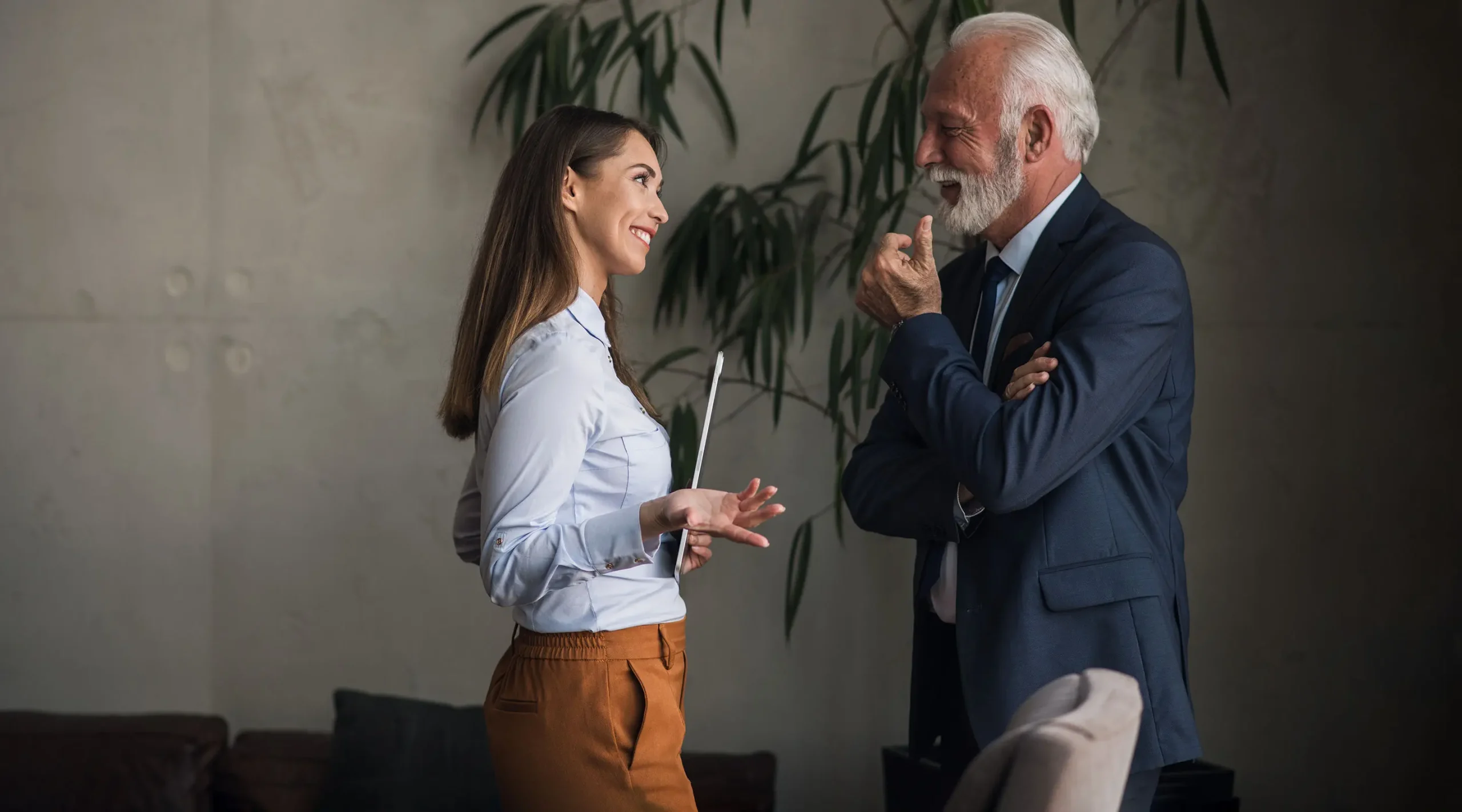 Asesora joven conversando con un cliente mayor en un entorno de oficina moderno.