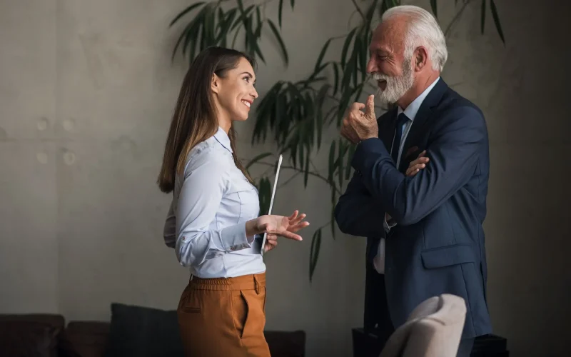 Asesora joven conversando con un cliente mayor en un entorno de oficina moderno.