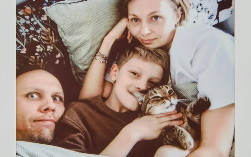 Familia formada por padre madre e hijo tumbados en el sofá abrazando a un gato atigrado.