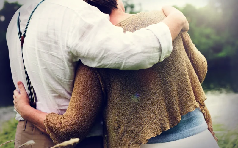 Pareja abrazada por la espalda en un entorno natural con árboles al fondo.