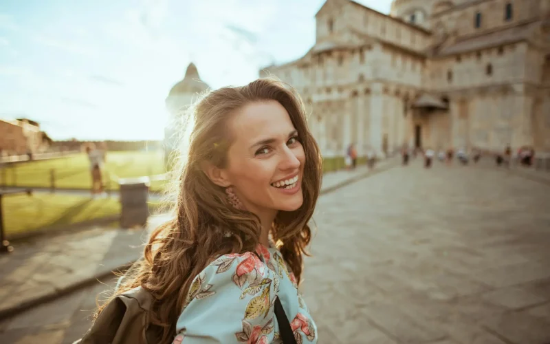 Turista joven sonriendo frente a una catedral histórica iluminada por el sol.